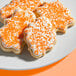 A plate of leaf-shaped sugar cookies decorated with white icing and coarse orange sanding sugar.