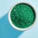 A bowl of Adourne Light Green sparkling sugar on a table.