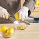 A person in a white coat uses a yellow Microplane zester to zest a lemon over a bowl.