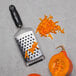 A Microplane black ultra-coarse grater next to a pile of shredded carrots on a counter.