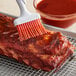 A brush applying red Pickapeppa Spicy Mango sauce to meat.