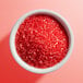 A white bowl filled with coarse red sanding sugar.