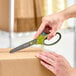 A person using 3M Scotch Non-Stick Pointed Tip Right-Handed scissors with green and dark gray handles to cut a box.