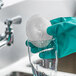 A gloved hand uses a 3M Scotch-Brite greener clean non-scratch scrubbing circle to clean a glass.
