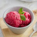 A bowl of pink Makai dragon fruit sorbet with mint leaves and a spoon.