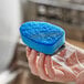 A hand holding a 3M Scotch-Brite blue non-scratch scrub pad.