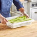 A person holding a white Choice food storage box filled with celery on a wooden surface.