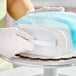 A white plastic fondant smoother being used to smooth blue marbled fondant on a cake.
