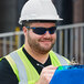 A man wearing 3M Scratch-Resistant Anti-Fog Safety Goggles with a black and blue frame and gray lenses holding a clipboard.