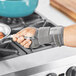 A person wearing a grey 3M Futuro Deluxe wrist stabilizer using a spoon to cook in a pan.