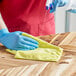 A person wearing blue gloves using a yellow 3M Scotch-Brite microfiber cloth to clean a surface.