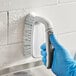 A person in blue gloves using a 3M Scotch-Brite all-purpose utility brush to clean a wall.