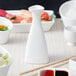 A white Whittier porcelain sake bottle on a white surface with red liquid in a white cup.