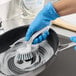 A white and blue scrubber brush with a curved handle being used to clean a soapy frying pan.