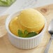A bowl of yellow Makai Mango Sorbet with mint leaves and a spoon.