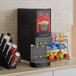 A black Curtis Cafe Series cappuccino machine on a counter with a cup of coffee and a sign.