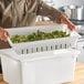 A man holding a white polyethylene food box with broccoli in it.