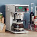 A Curtis commercial coffee maker on a counter with a bottle of coffee.