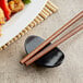 A black bowl chopstick rest with chopsticks on a table in an Asian restaurant.