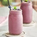 Two glasses of pink Makai Organic Unsweetened Acai smoothie with straws on a table.
