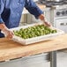 A man in a chef's uniform holding a white Choice food storage box on a counter in a salad bar.