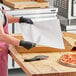 A woman in a pink apron and black gloves using a Choice dry wax paper to hold a pizza slice.