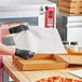 A person wearing black gloves is cutting a pizza on a Quilon-coated pizza box liner on a kitchen counter.