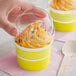 A hand holding a plastic lid over a yellow Choice paper cup of frozen yogurt with sprinkles.