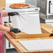 A person in a black apron and gloves using a Quilon-coated paper to open a pizza box.