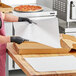 A woman in a black apron cutting pizza on white dry wax paper.