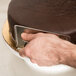 A hand using an Ateco stainless steel fondant smoother to smooth chocolate fondant on a cake.