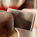 A person using a silver rectangular Ateco stainless steel fondant smoother to smooth chocolate fondant on a cake.