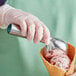 A person in gloves holding a Choice Aluminum Green Ice Cream Scoop filled with ice cream.