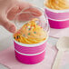 A hand holding a Choice pink and white paper cup of frozen yogurt with a plastic lid over it.