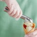 A hand in a glove using the Choice aluminum ice cream scoop to serve ice cream in a waffle cone.