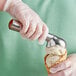 A hand in a glove holding a gold aluminum ice cream scoop filled with ice cream.