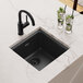 A Zurn Elkay black quartz sink in a white countertop with a glass of ice and lime slices.