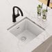 A Zurn Elkay white quartz bar sink with a hole in it over a counter with two glasses and a glass of water with ice and lime slices.