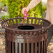 A woman using a pink cloth to clean a brown Lancaster Table & Seating flat lid on a trash can.