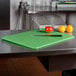 A San Jamar green cutting board on a counter with a knife and fruits.