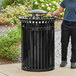 A man standing next to a Lancaster Table & Seating black steel outdoor trash can.