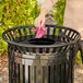 A woman using a pink cloth to clean a black Lancaster Table & Seating trash can.