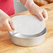 A person in gloves holding a round white Quilon parchment liner in a metal pan.