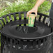 A hand putting a cup into a Lancaster Table & Seating black round flat lid for a trash can.