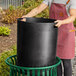 A woman in a pink apron holding a Lancaster Table & Seating black plastic round can liner.