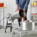 A man pouring red sauce from an Avamix electric blender into a large pot.