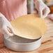 A person in gloves placing a Baker's Lane round parchment liner in a metal pan.