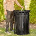 A man standing next to a Lancaster Table & Seating black steel slatted outdoor trash can with a flat lid.