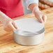 A person wearing gloves using a Baker's Lane Quilon coated parchment pan liner in a round cake pan.