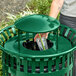A person putting a plastic cup with a straw into a green Lancaster Table & Seating trash can lid.
